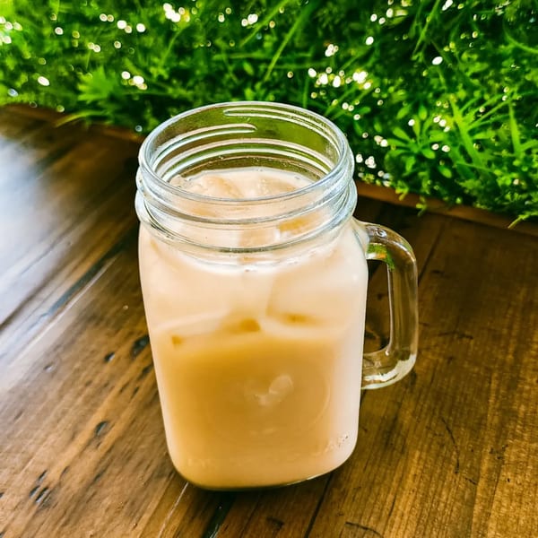 Horchata in a mason jar with ice, on a wooden table with green foliage in the background.