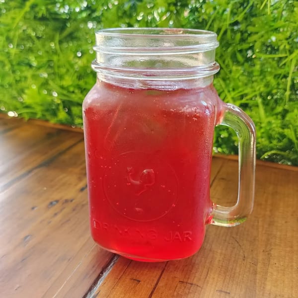 A vibrant red Mexican drink in a mason jar, condensation on the glass, on a wooden table.