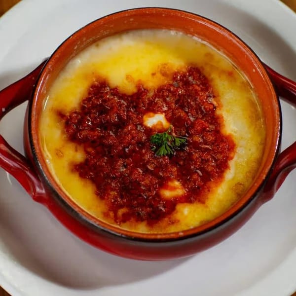 Melted yellow cheese dip with red chorizo and a sprig of cilantro in a red bowl.
