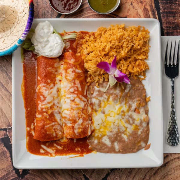 Pueblita Mexican Restaurant's enchiladas with rice, beans, sour cream, and a purple orchid garnish.