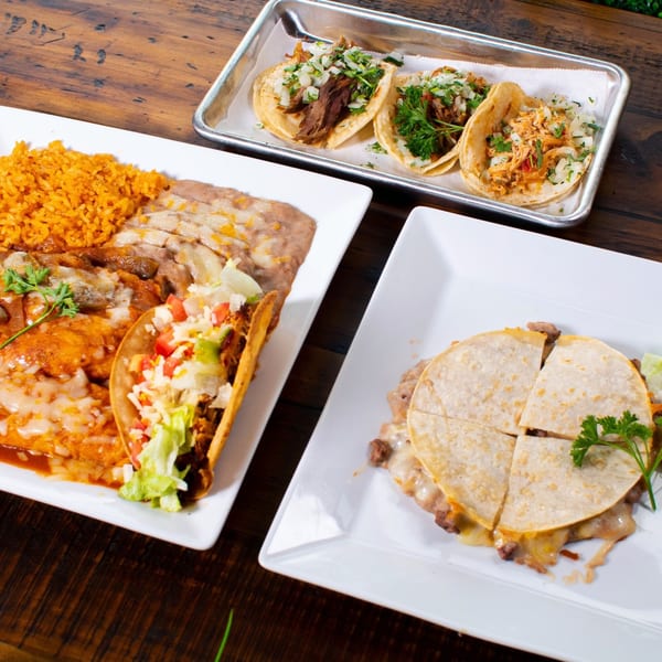 Plates of Pueblita Mexican Restaurant's tacos, enchiladas with rice and beans, and a quesadilla on a wooden table.