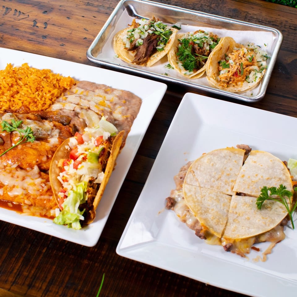 Plates of Pueblita Mexican Restaurant's tacos, enchiladas with rice and beans, and a quesadilla on a wooden table.